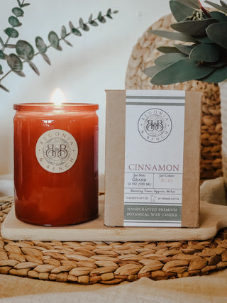 A red glass jar candle burning next to the kraft packaging in scent of cinnamon.