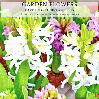 Close-up image of a floral arrangement featuring white gardenias, cream-colored tuberoses, and various shades of pink lilies. The flowers are surrounded by green leaves.