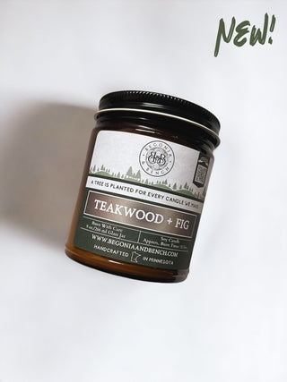 A 9oz amber jar candle labeled "Teakwood & Fig™ - By Begonia & Bench®" is shown. The label mentions the soy candle is handcrafted in Minnesota. Text on the top right corner reads "New!" The label also includes a QR code and website: www.begoniaandbench.com. The fall candle sits on a white background.