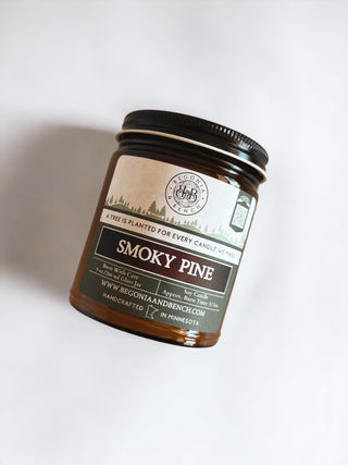 Introducing the handcrafted "Smoky Pine™" 9oz. amber jar candle by Begonia & Bench®. This fall-scented candle features a bicycle logo and the inspiring message "A Tree is Planted for Every Candle We Make." Made in Minnesota, this eco-friendly product can be found at www.bergoniaandbench.com for more details.