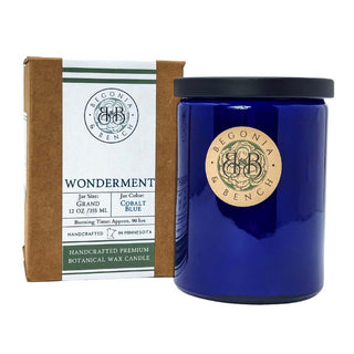 A cobalt blue candle jar with a black lid is shown, featuring a copper logo label of "Begonia & Bench®." The fall candle is placed next to its brown packaging box, which displays the text "Wonderment™ - 12oz Finely Crafted Scented Candle," jar size "Grand 12 oz / 355 mL," jar color "Cobalt Blue," and indicates a burning time of approximately 90 hours.