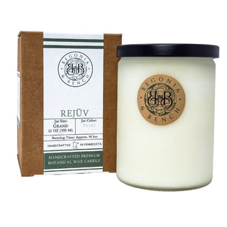 A white scented candle in a frosted glass jar with a black lid sits next to a brown and white box. Both the jar and the box feature labels for "Begonia & Bench®" and their product "Rejüv™ - 12oz Finely Crafted Scented Candle." The label indicates the jar size is 12 oz, with an approximate burning time of 90 hours.