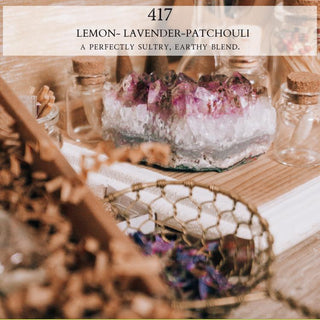 A tabletop scene displays a crystal with purple and white hues on a wooden surface, surrounded by small glass jars with cork stoppers and various dried herbs. A net and wooden objects add to the earthy, rustic setting. The text at the top reads, “417™ - 12oz Finely Crafted Scented Candle By Begonia & Bench®: A perfectly sultry, earthy blend.”