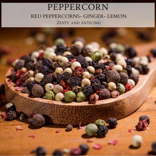 A wooden bowl filled with an assortment of colorful peppercorns, including red, green, white, and black varieties, rests on a wooden surface. The image is overlaid with text that reads: "Peppercorn - 12oz Finely Crafted Scented Candle By Begonia & Bench® - Zesty and enticing like a fall candle.