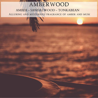 Background: A serene sunset over a calm lake with a distant shoreline. In the foreground, a blurred silhouette of a boat and a hanging palm frond add to the tranquil scene. Text reads: "Amberwood - 12oz Finely Crafted Scented Candle By Begonia & Bench®. Amber - Sandalwood - Tonkabean. Alluring and mysterious fragrance of amber and musk.