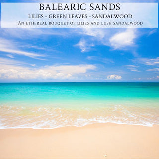 A serene beach scene with a sandy shore, gentle white waves, and a calm turquoise sea under a blue sky with light clouds. The text on the image reads: "Balearic Sands™ - Lilies - Green Leaves - Sandalwood. An ethereal bouquet of lilies and lush sandalwood in our 12oz finely crafted scented candle by Begonia & Bench®.