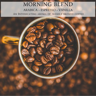 A close-up image of a cup filled with coffee beans. The cup has a golden handle and sits on a blurred background of more coffee beans. Text above the cup reads: "MORNING BLEND™ - 12oz Finely Crafted Scented Candle By Begonia & Bench®." An intoxicating aroma reminiscent of the coziest fall candle fills the air.