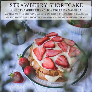 A round Strawberry Shortcake by Begonia & Bench®, adorned with sliced strawberries and cream, is elegantly presented on a plate, encircled by fresh strawberries. The background features a subtle blur accentuated by the warm glow of a Strawberry Festival candle, which fills the air with its artisan-crafted fragrances, creating an inviting and aromatic atmosphere.