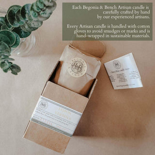 The image displays a Citrus & Clove™ - 12oz Finely Crafted Scented Candle by Begonia & Bench®, partially unboxed. The box and candle are accompanied by a care instruction leaflet. A green leafy plant is visible on the left. A text overlay emphasizes the handmade quality and sustainable packaging of these fall candles.