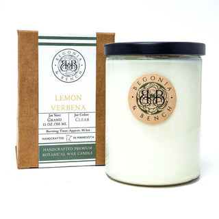A finely crafted lemon verbena scented candle from Begonia & Bench® rests in a clear jar with a black lid beside its brown and green packaging box. The box reads "Begonia Bench, Lemon Verbena, Grand Size 12 oz, 355 ml, Burning Time Approx. 90 hrs" and "Handcrafted in Minnesota." Both the jar and box feature a wooden emblem displaying the brand logo.