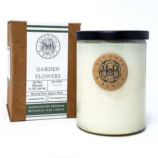 A Garden Flowers™ - 12oz Finely Crafted Scented Candle by Begonia & Bench® in a clear glass jar with a black lid. The label features the brand logo and the packaging specifies the scent as "Garden Flowers," with a size of 12 oz/355 ml and an approximate burning time of 90 hours.