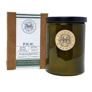 Image shows a P.N.W. - 12oz Finely Crafted Scented Candle by Begonia & Bench®. This fall candle, scented with natural botanicals, comes in a vintage green 12 oz glass jar with a black lid. The label on the brown box provides details about the jar size, color, and an approximate burning time of 90 hours. Handcrafted in Minnesota.